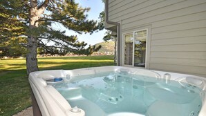 Ein Whirlpool im Freien neben einem Haus mit Rasen und Bäumen.