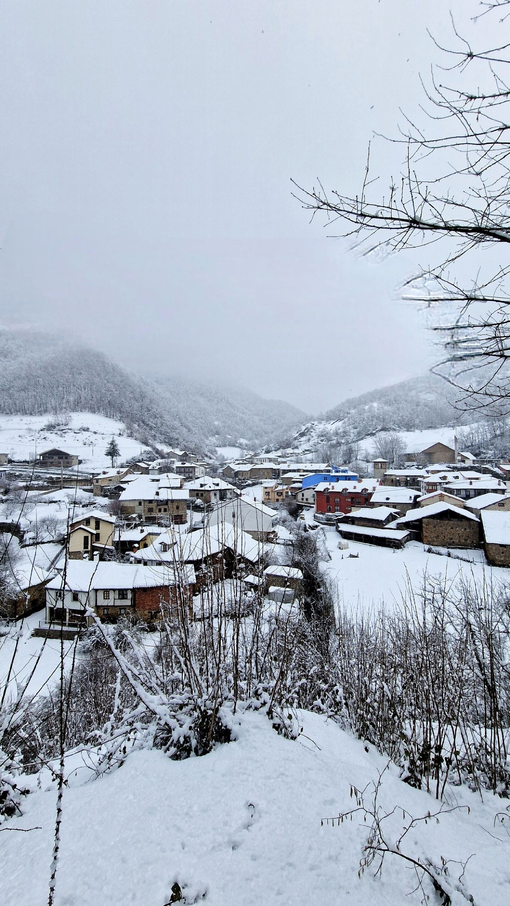 Un village enneigé, avec des bâtiments traditionnels et une chaîne de montagnes en arrière-plan.