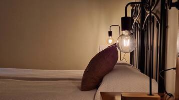 A neatly made bed with a textured white duvet, a single brown pillow, and a bedside table with a book and a lamp.