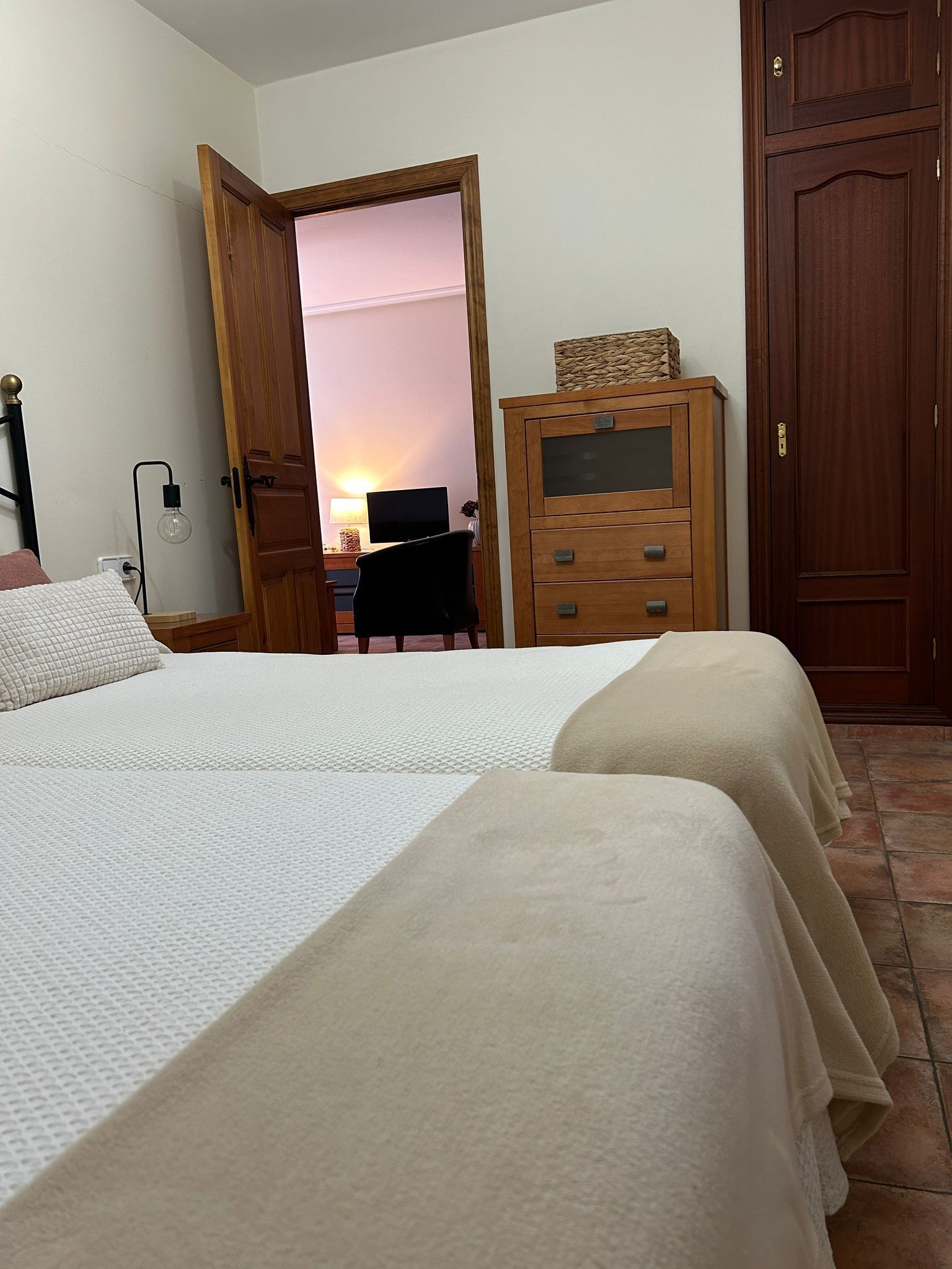 Ein Schlafzimmer mit zwei Betten, einer Holzkommode und einem Schreibtisch mit einem Computer.