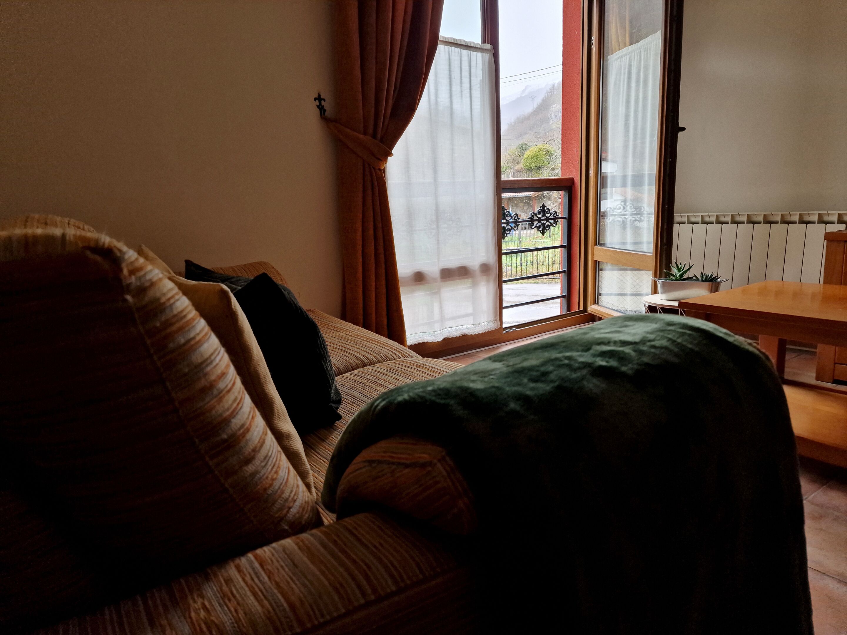 A cozy room with a sofa, a wooden table, and a view of a garden through a window.