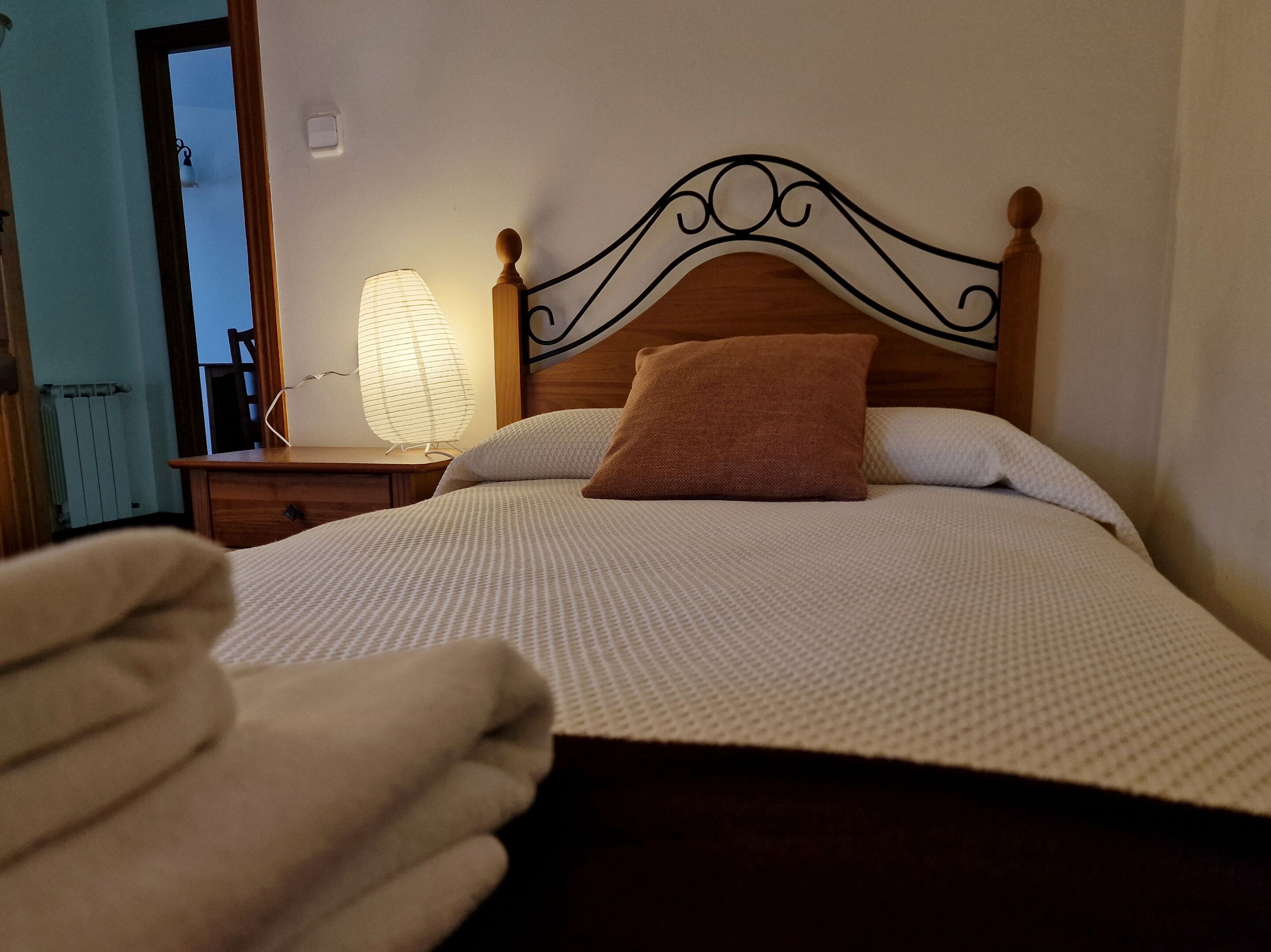 Una cama bien hecha con cabecera de madera, una lámpara de noche y un cojín marrón.