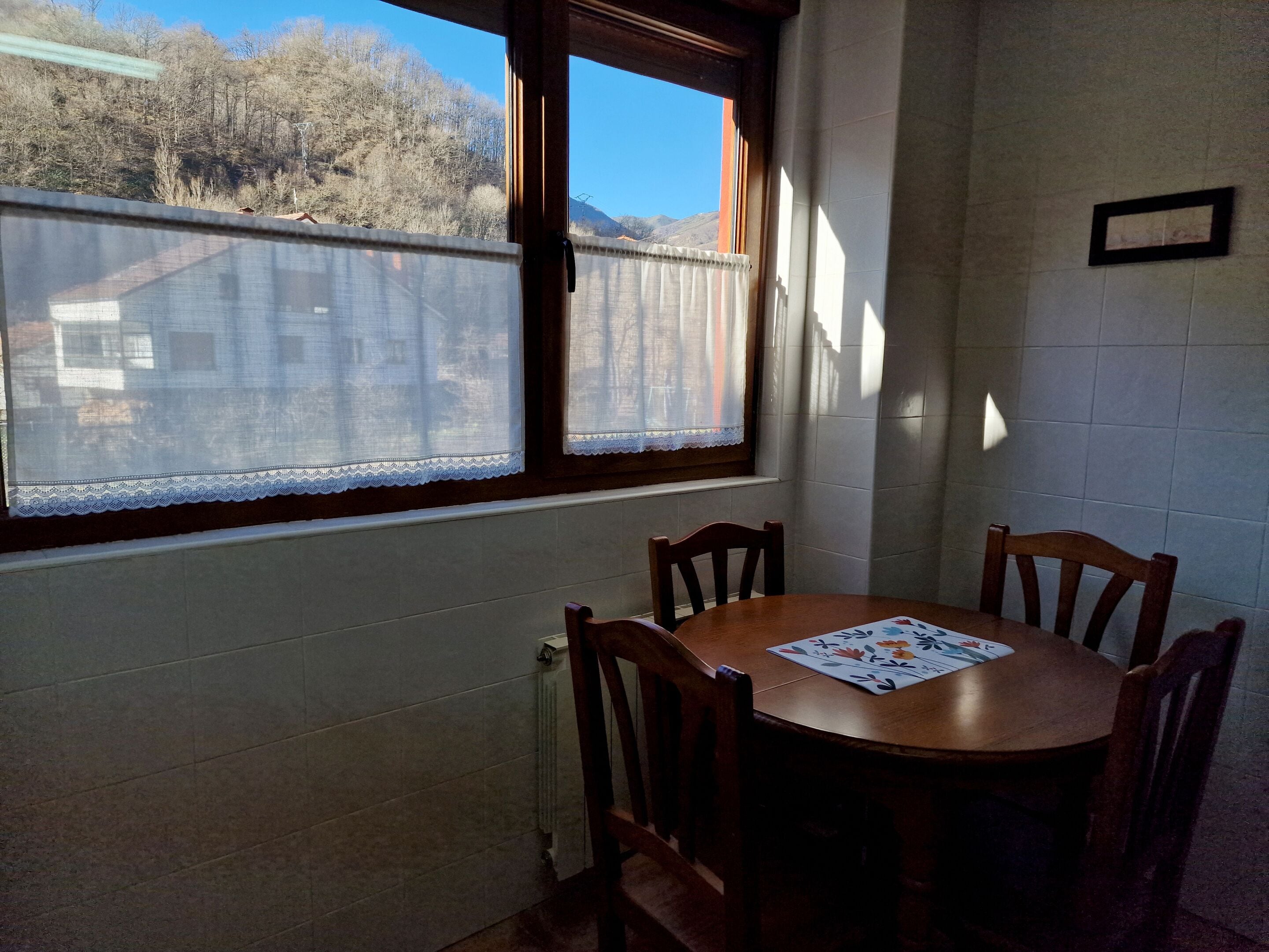 Un comedor con una mesa redonda y cuatro sillas, una ventana con cortinas de encaje y un radiador debajo de la ventana.