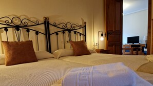 Una cama bien tendida con un cabecero decorativo, una mesita de noche con una lámpara y un televisor al fondo.