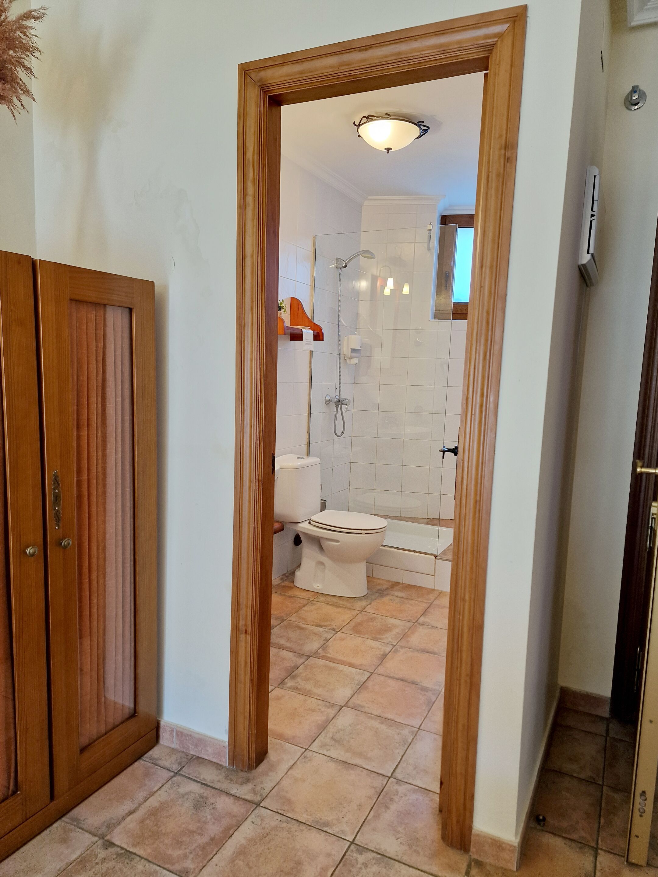 A bathroom with a toilet, shower, and bathtub, a wooden door frame, and tiled flooring.