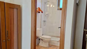 A bathroom with a toilet, shower, and bathtub, a wooden door frame, and tiled flooring.