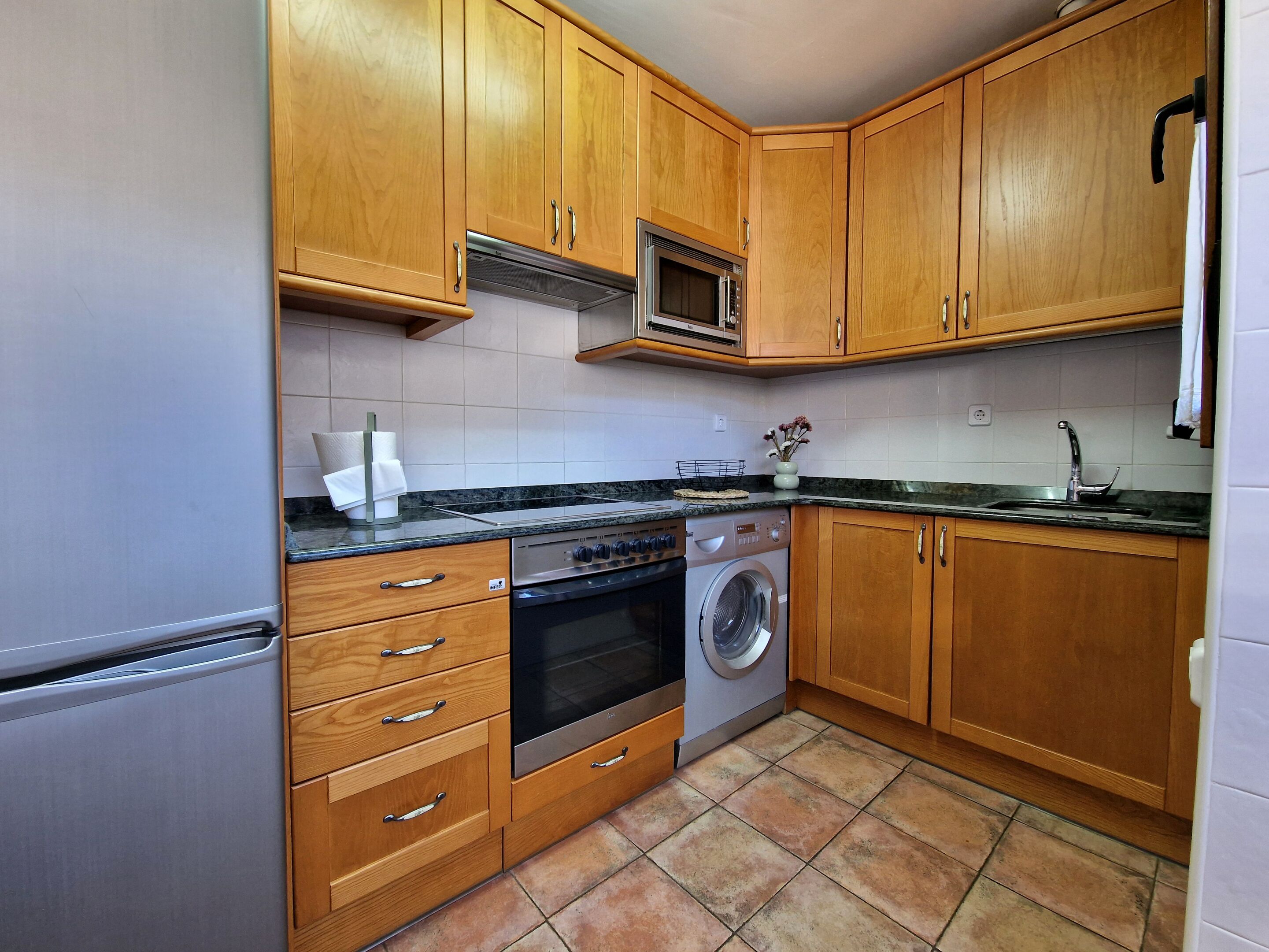 Una cucina con mobili in legno, un forno a microonde, un piano cottura, una lavatrice e un lavello.
