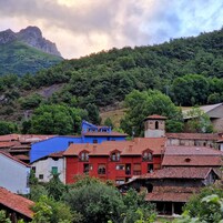 Un pueblo con techos rojos tradicionales, un edificio azul destacado y una montaña al fondo.