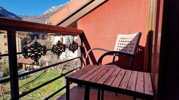 A balcony with a wooden table and a metal chair, overlooking a mountainous landscape.