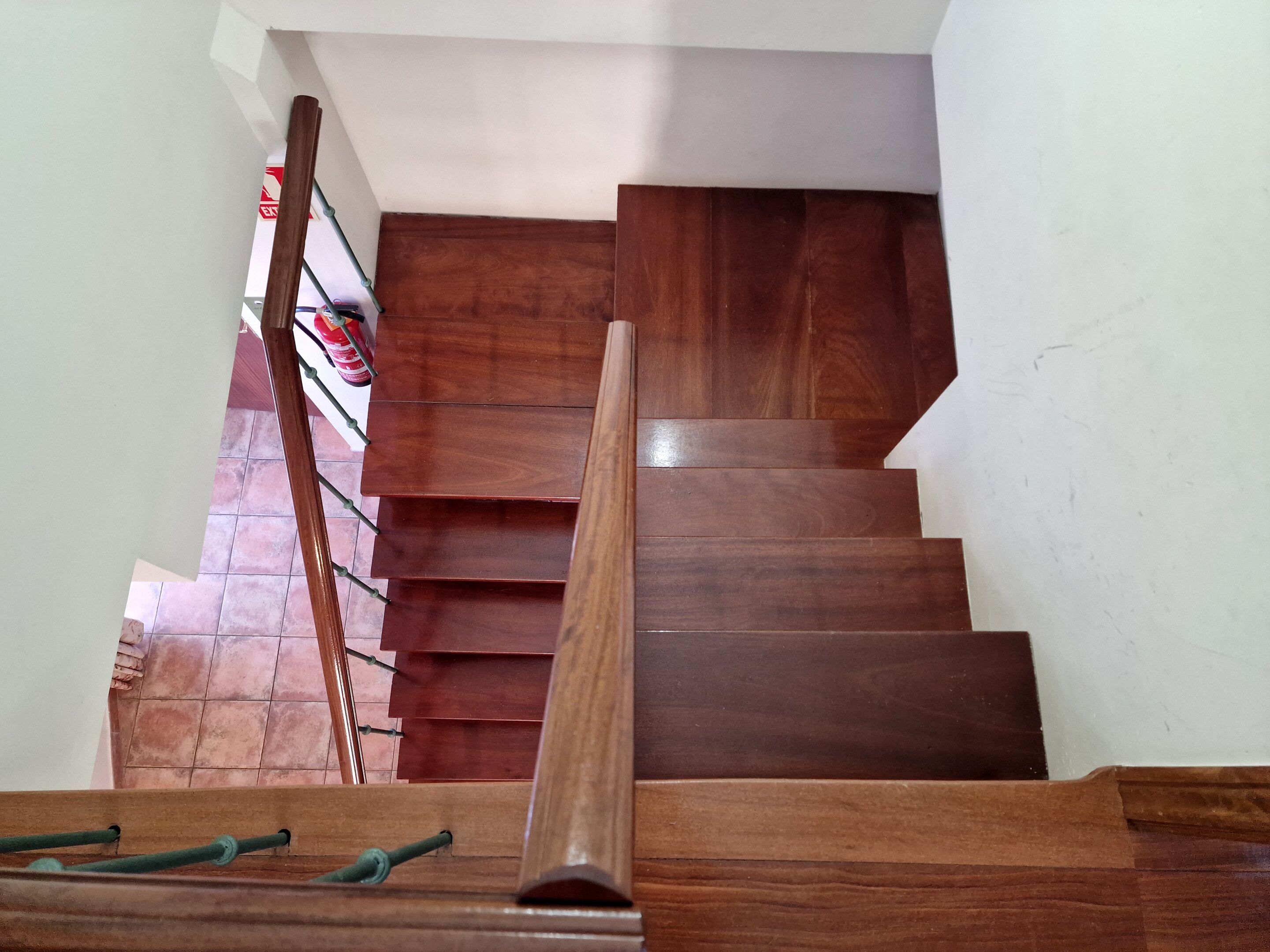 A wooden staircase with a handrail, leading to a landing with a red fire extinguisher and a white wall.