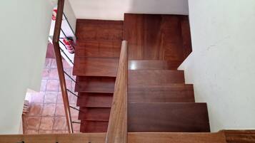 A wooden staircase with a handrail, leading to a landing with a red fire extinguisher and a white wall.