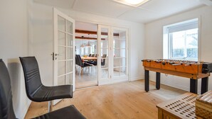 Une pièce avec un plancher en bois, une table de baby-foot, une table à manger avec des chaises et une grande fenêtre.