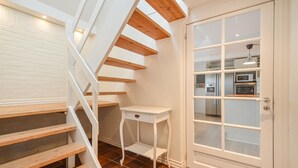 Un escalier avec des poutres en bois, une porte blanche avec des panneaux de verre et une petite table blanche.