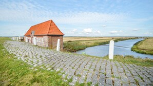 Un bâtiment en briques avec un toit rouge, un chemin pavé et une rivière en arrière-plan.