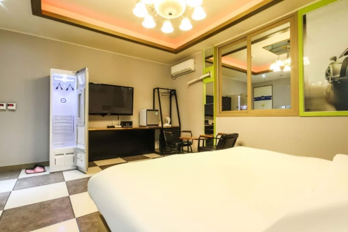 A hotel room with a large bed, a desk with a computer, a TV, and a mirror.