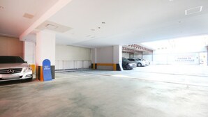 A parking garage with a Mercedes-Benz SUV parked in the foreground, a blue sign, and a white car in the background. - Blue Motel (Gwangju)