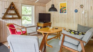 Una sala de estar acogedora con televisor, muebles de madera y ventana con vistas a la vegetación.