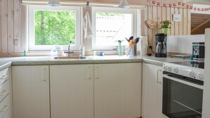 Una cocina con encimera de granito, armarios blancos, un lavamanos, una estufa y una ventana con vistas a la vegetación.