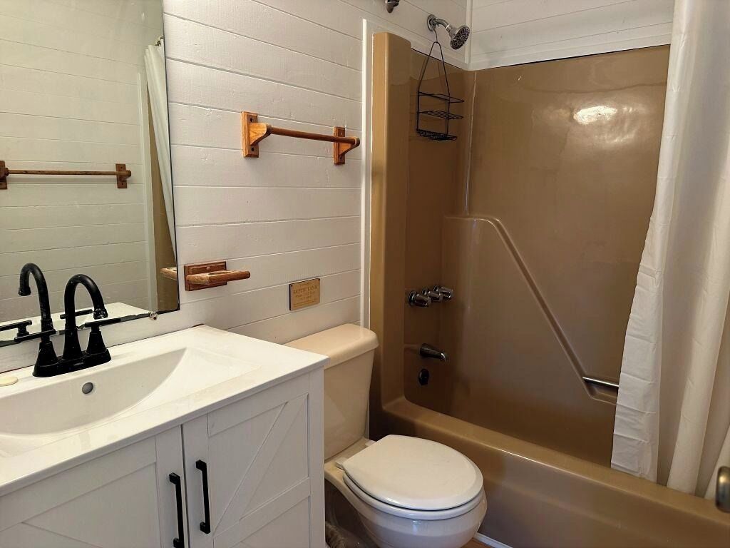 A bathroom with a white sink, black faucet, wooden towel rack, and a beige bathtub with a shower curtain.