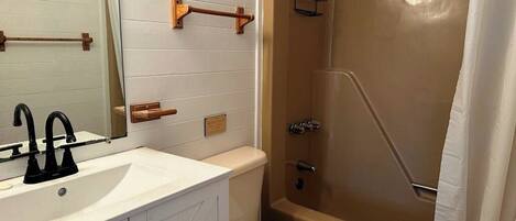 A bathroom with a white sink, black faucet, wooden towel rack, and a beige bathtub with a shower curtain.