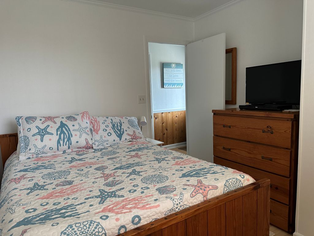 Une chambre à coucher avec un lit, une commode en bois et un téléviseur.