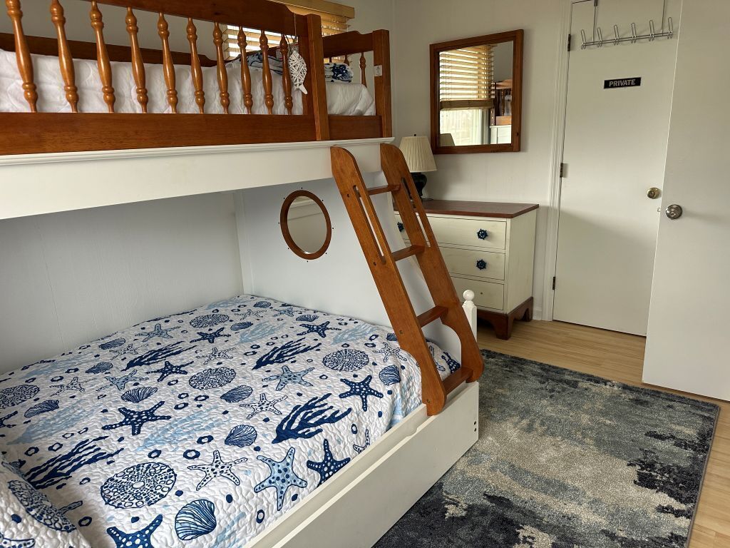 A bunk bed with a wooden ladder, a round mirror, a dresser with drawers, and a private door.