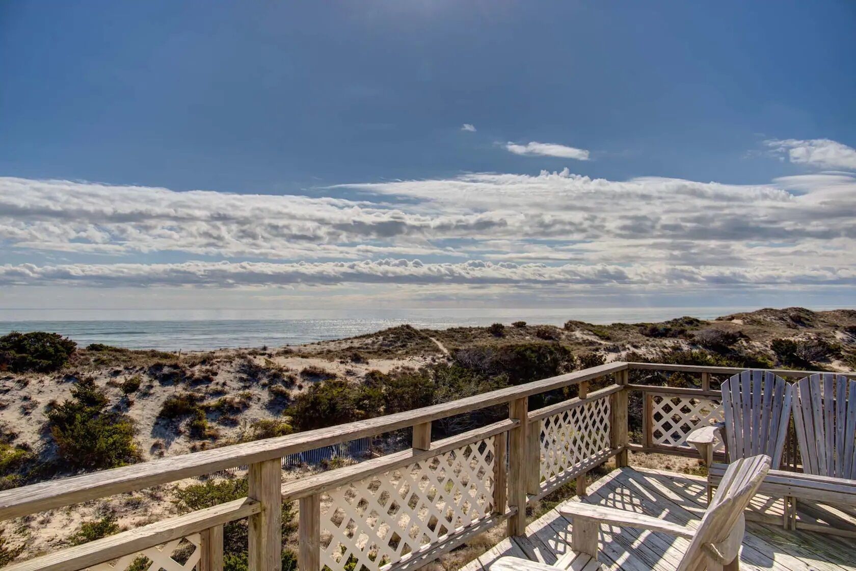 Una terraza de madera con vista a la playa y las dunas.