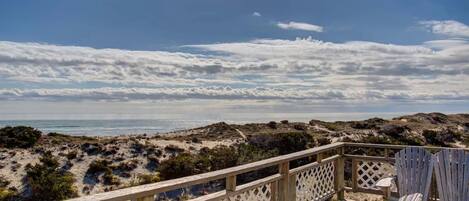 A wooden deck with a view of the beach and dunes.