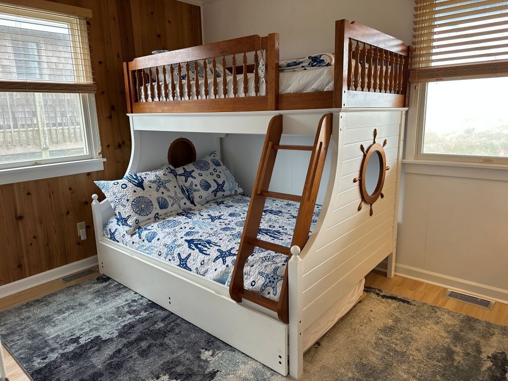 Un lit superposé avec une échelle, une fenêtre ronde et une couvre-lit à motifs.