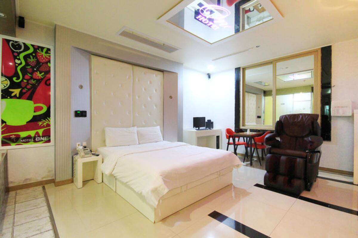 A hotel room with a large bed, a desk, a chair, a massage chair, and a large mirror.