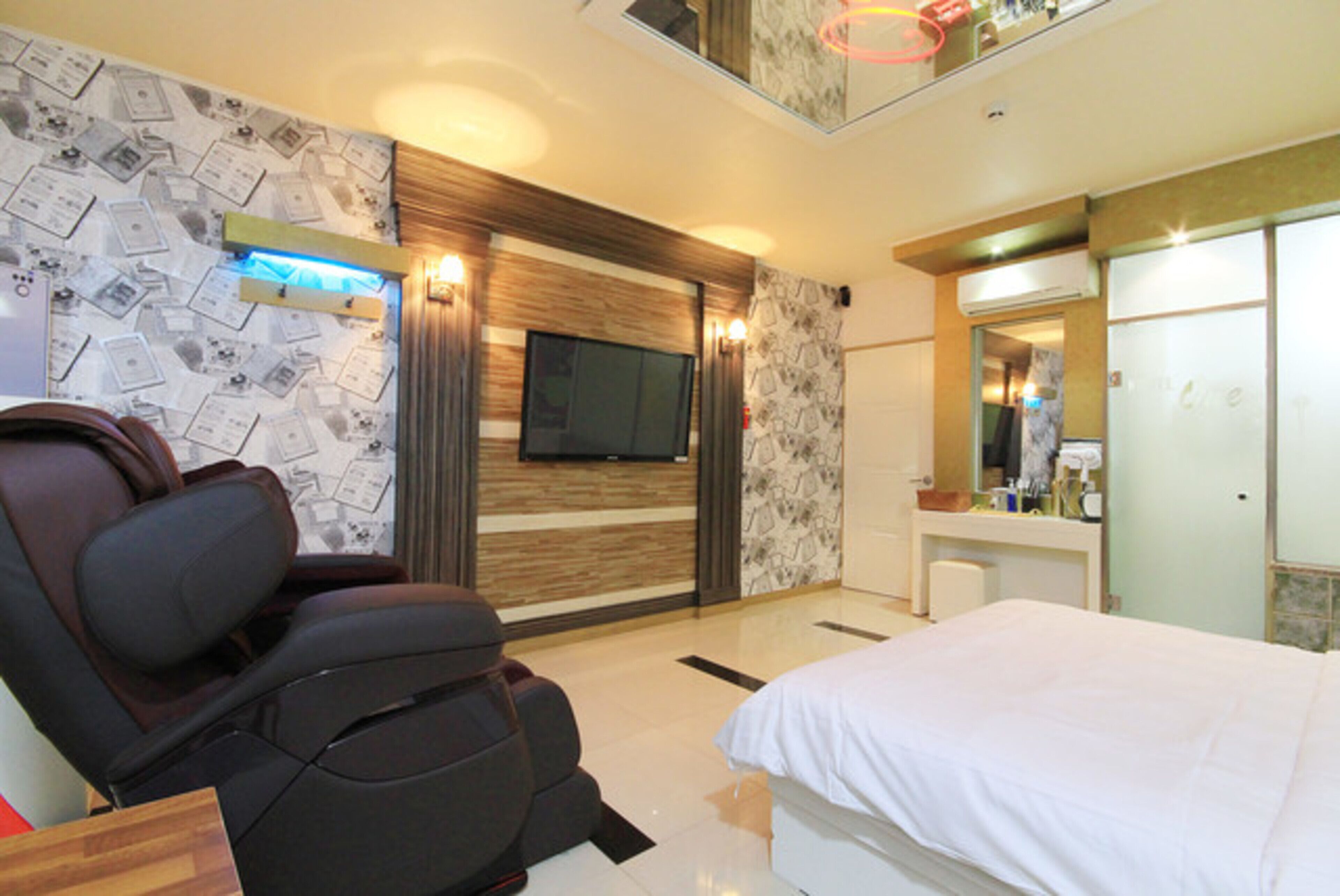 Une chambre d’hôtel moderne équipée d’un fauteuil massant, d’un téléviseur à écran plat, d’un grand lit, d’une coiffeuse avec miroir et d’un téléviseur fixé au mur.