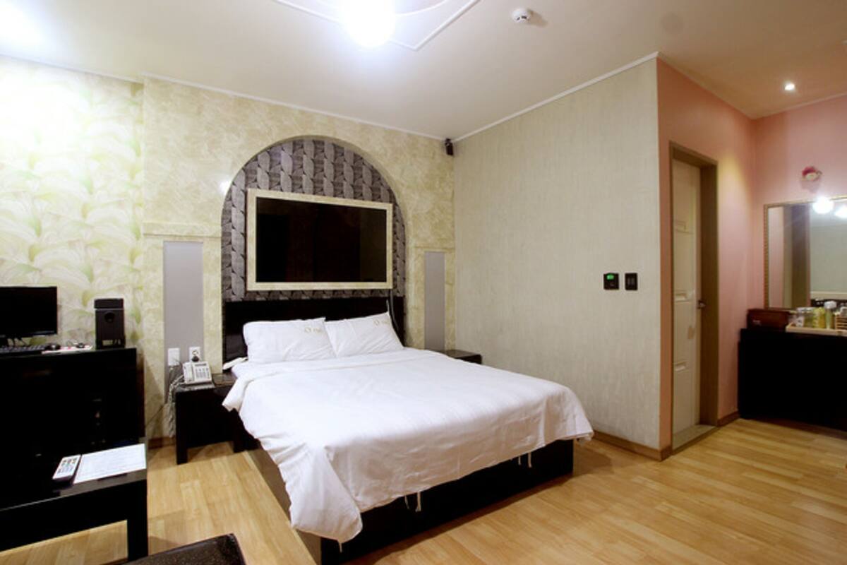 A hotel room with a large bed, a TV, a desk, and a mirror.