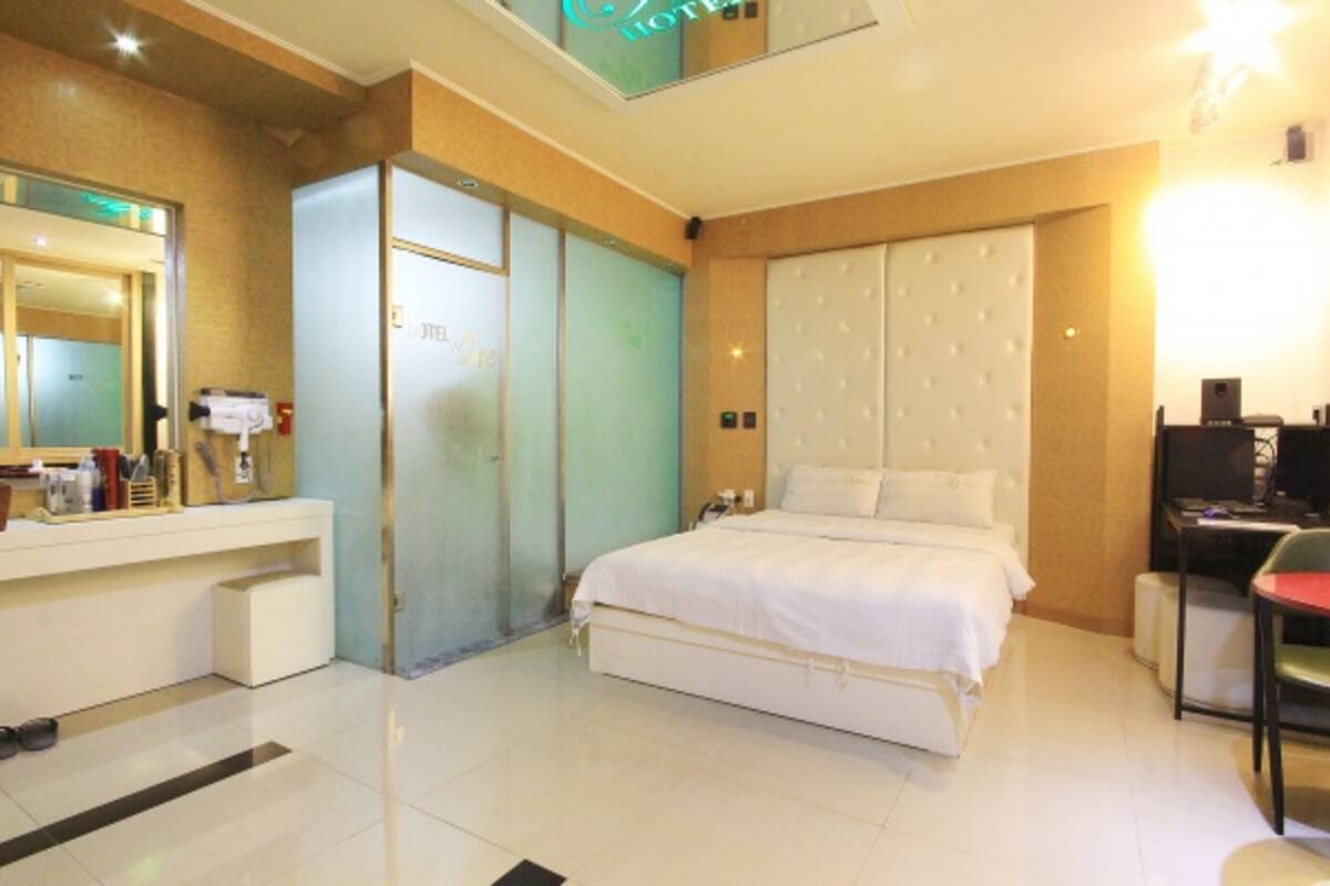 A hotel room with a bed, a desk, a chair, a mirror, and a wardrobe.