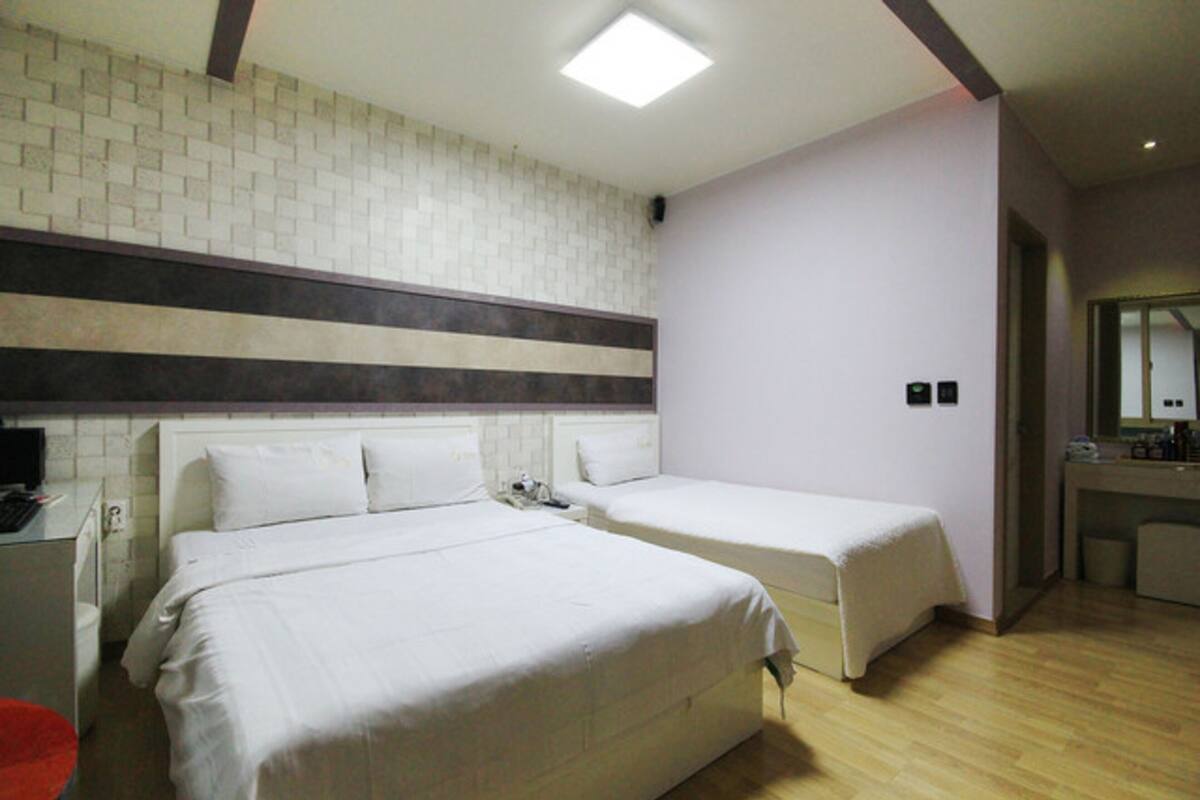 A hotel room with two beds, a desk, a chair, a small table, and a mirror.