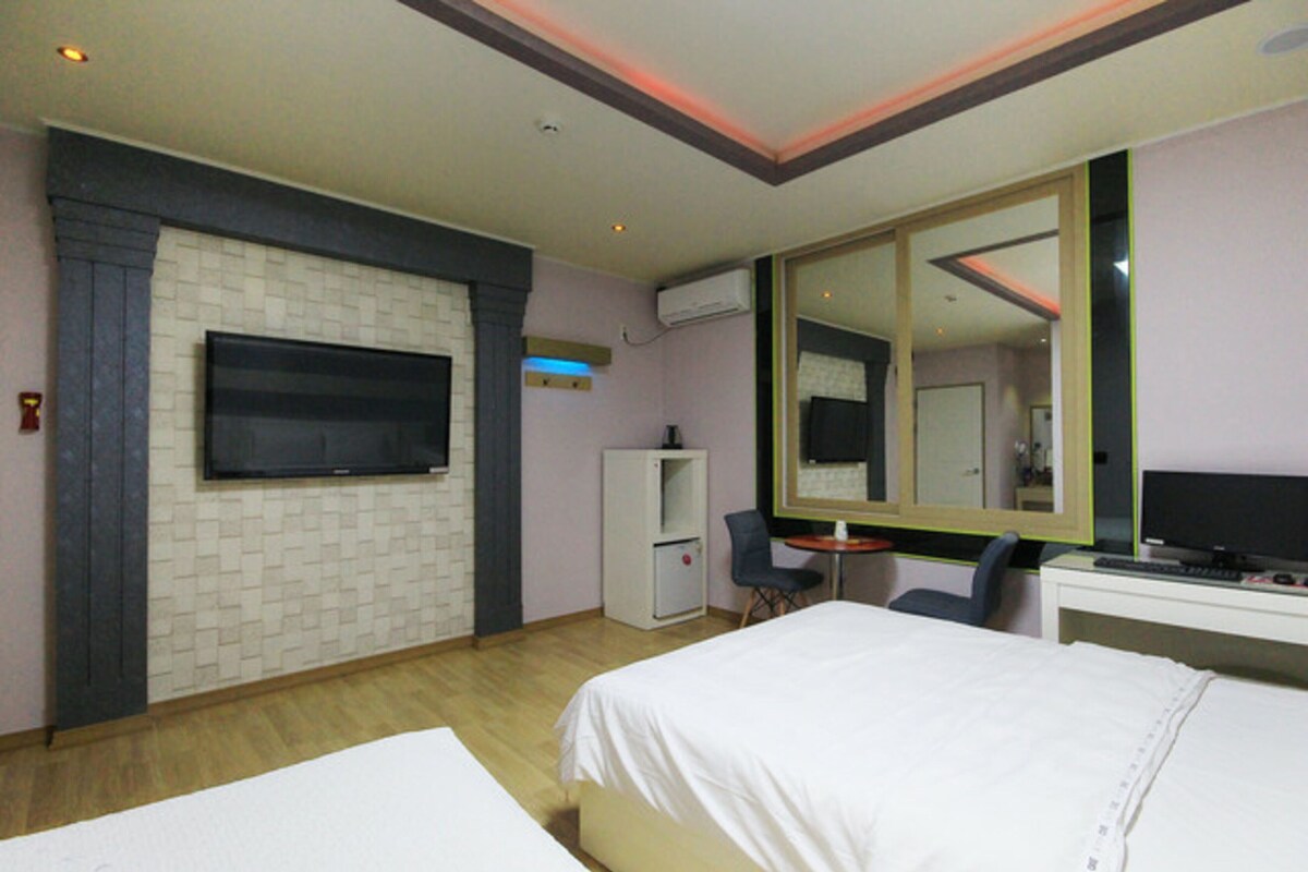 A hotel room with a bed, a desk, a chair, a television, a mirror, and a small cabinet.