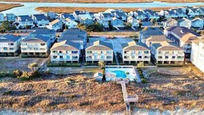 A coastal residential area with multiple two-story houses, a swimming pool, and a dock leading to a beach. - Oceanfront Complex with Ocean Views. (Ocean Isle Beach)