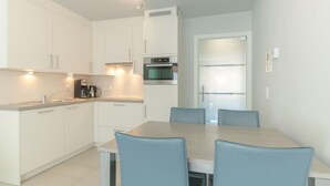 A modern kitchen with white cabinets, a built-in oven, and a dining area with a table and chairs. - Seaside 101 with parking by Interhome (Bredene)