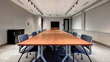 A conference room with a long table, chairs, a projector screen, and a carpeted floor.