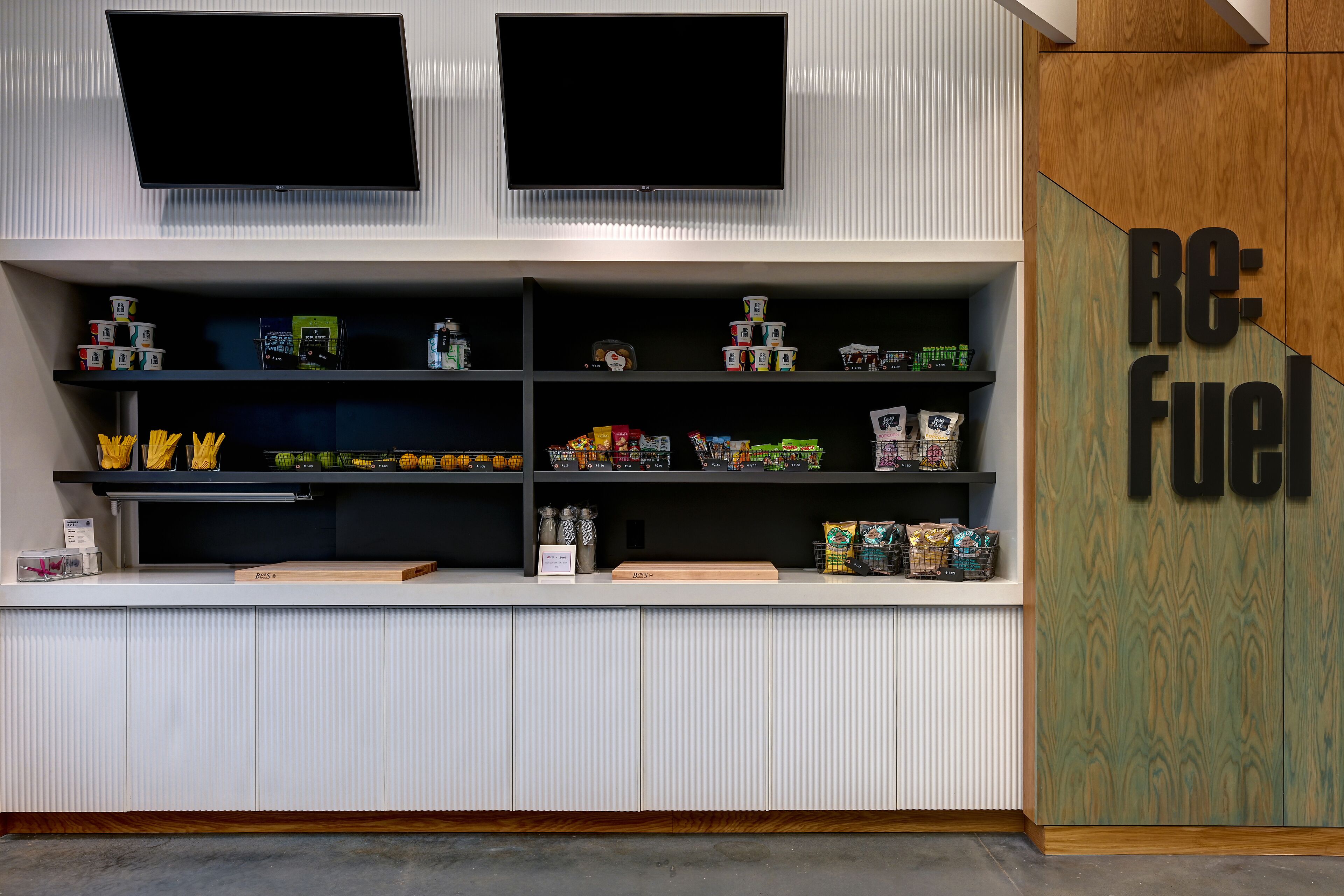 Zona de recepción con mostrador que exhibe varios productos, un televisor montado arriba y un panel de madera con el texto "Re-Fuel".