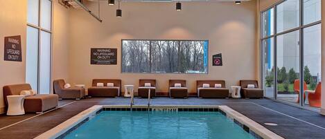 A modern indoor pool area with lounge chairs and a view of trees through large windows.