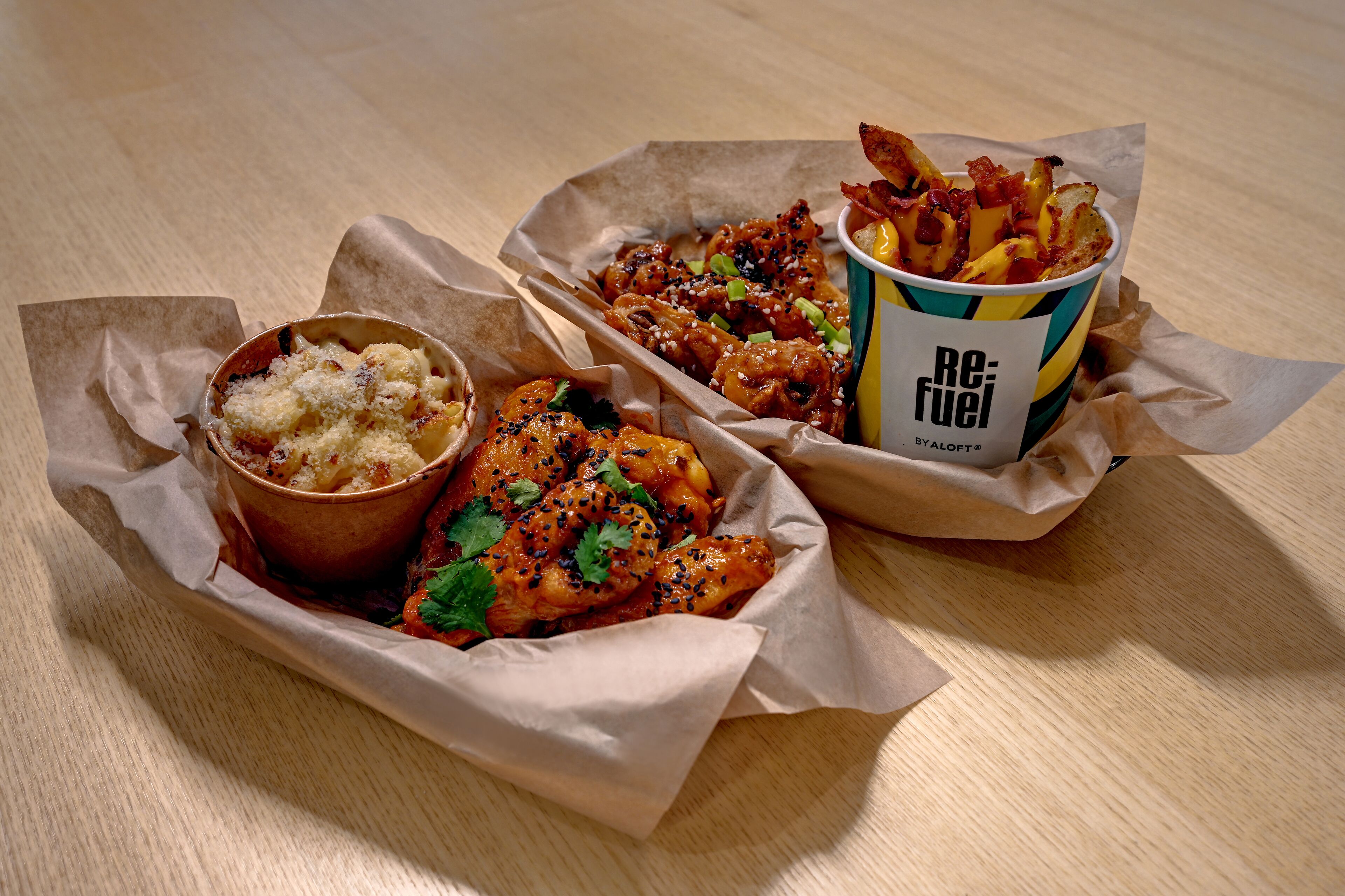 A meal consisting of a chicken dish, fries, and a dessert in paper containers on a wooden table.