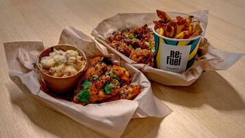 A meal consisting of a chicken dish, fries, and a dessert in paper containers on a wooden table.