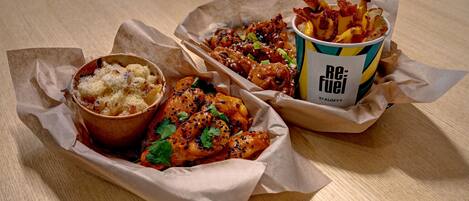 Un plato de pollo, papas fritas y un postre en recipientes de papel sobre una mesa de madera.