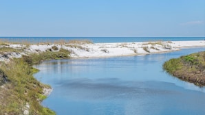 Ein Fluss schlängelt sich durch eine sandige Landschaft mit spärlicher Vegetation und einem wolkenlosen Himmel.