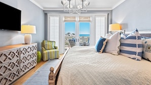 Ein Schlafzimmer mit Bett, Fernseher, einer Kristallleuchter und Meerblick, inklusive Balkon.
