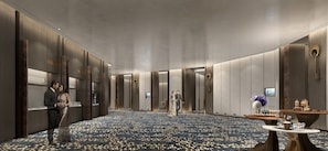 Un hall de hotel amplio y moderno, con alfombra circular, paneles de madera y una mesa central con refrigerios.