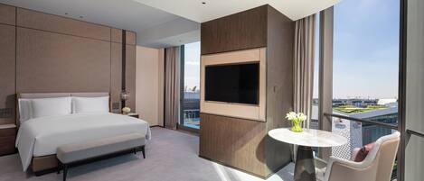 Een moderne hotelkamer met een groot bed, een flatscreen televisie aan de muur, een klein rond tafeltje met een bloemenvaas en een stoel.