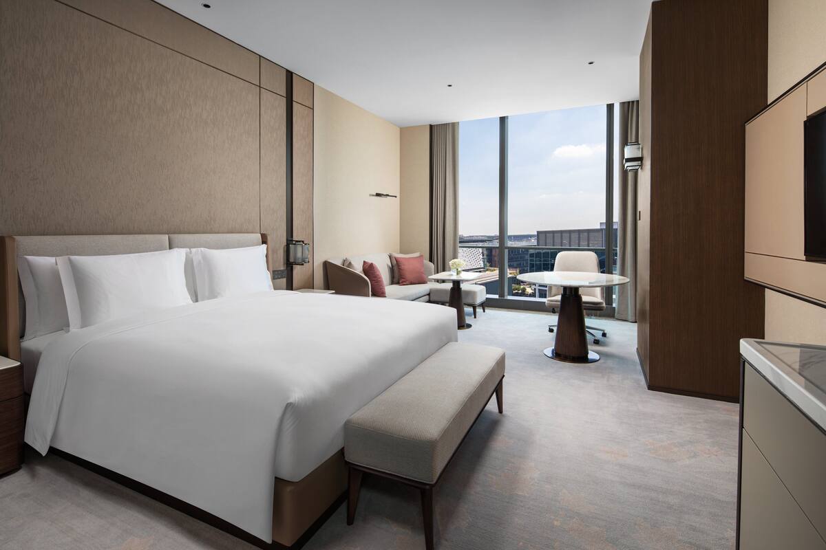 Ein modernes Hotelzimmer mit einem großen Bett, einer Sitzecke mit Tisch und einem Fernseher.