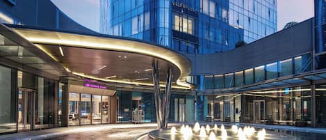 Un edificio moderno con fachada de vidrio, una fuente central y un letrero que dice 'CROWNE PLAZA'.