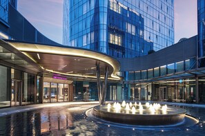 Un bâtiment moderne doté d’une façade en verre, d’une fontaine centrale et d’une enseigne indiquant « CROWNE PLAZA ».